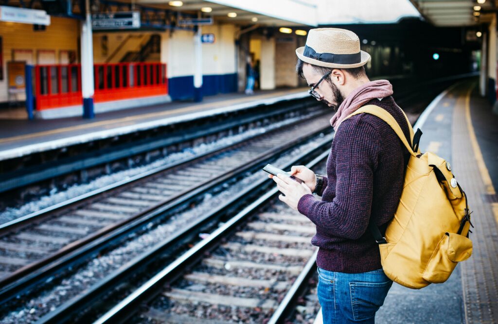 Man with backpack uses phone at urban train station platform.