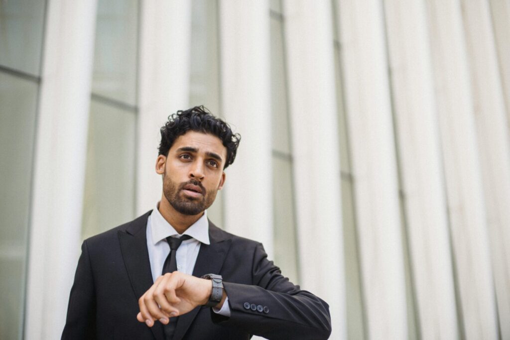 A professional man in a suit checks the time on his watch while standing outside, capturing a business theme.