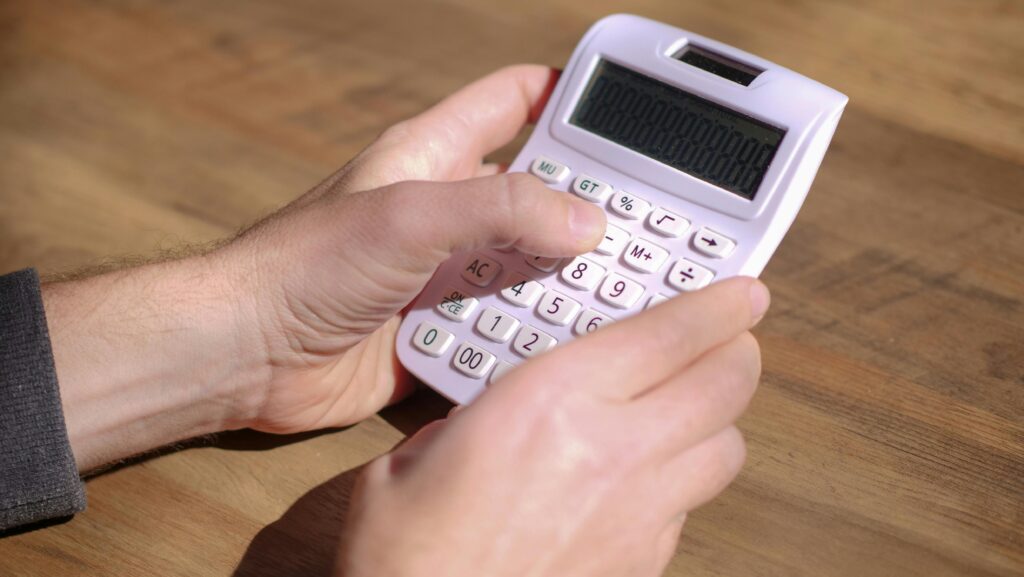 Hands using a pink calculator on a wooden table, emphasizing calculation and mathematics.