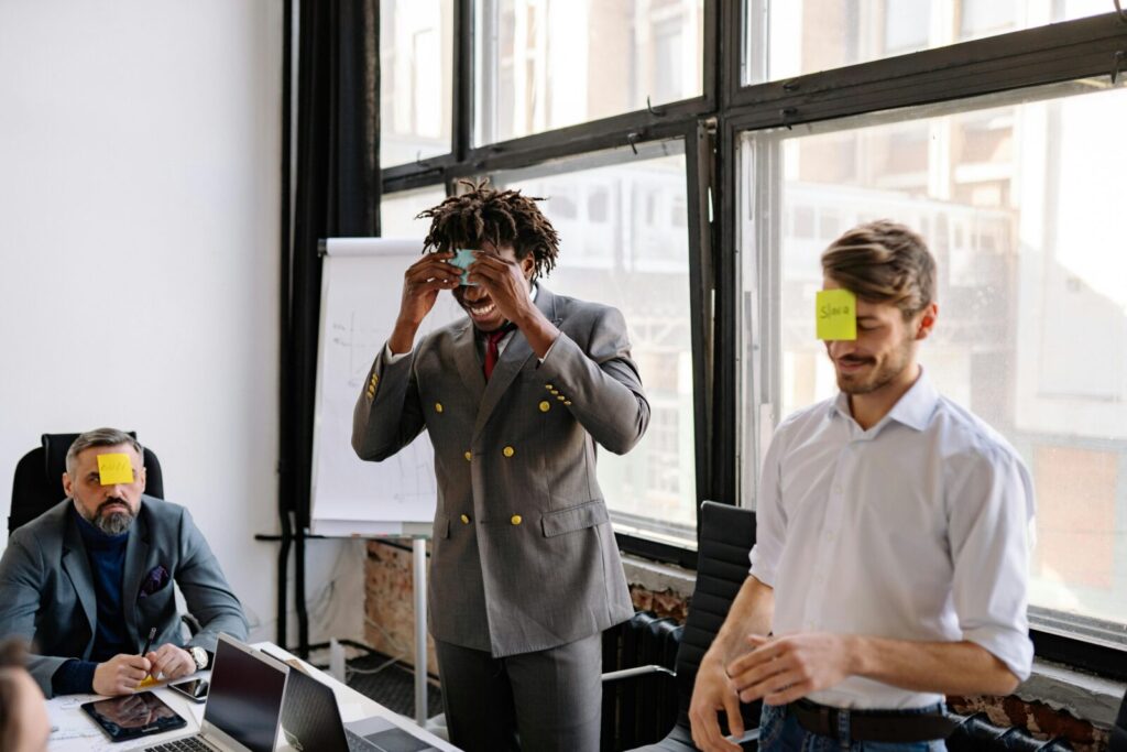 Office workers enjoy a lively team-building exercise with sticky notes on foreheads, fostering collaboration.