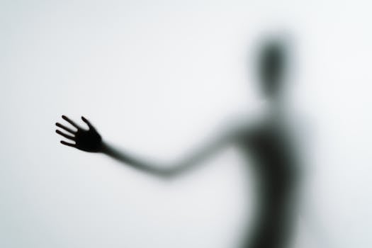 Blurred silhouette of a hand reaching out against a light background in an abstract style.